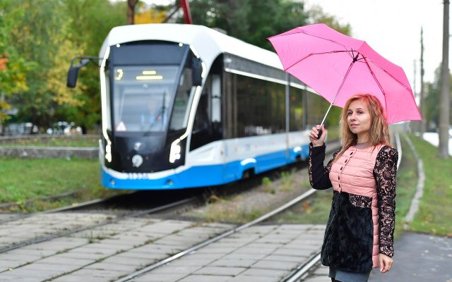 雨夜公交站台，一名乘客独自撑伞等车，路灯在水洼里拉出长长的光条